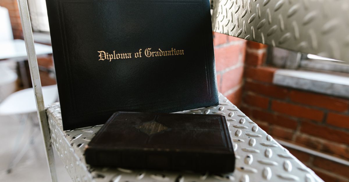 Close-up of a diploma and book on a metal staircase indoors, symbolizing academic achievement.